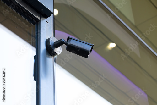 Security camera mounted on a glass wall, capturing surveillance footage in a modern commercial building with soft lighting and a sleek design