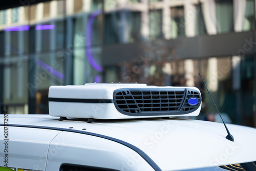 Photos White vehicle with rooftop air conditioning unit parked in urban setting, modern