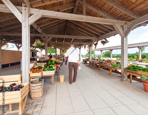 An outdoor market with produce, wooden stalls, and a person walking toward a landscape view
