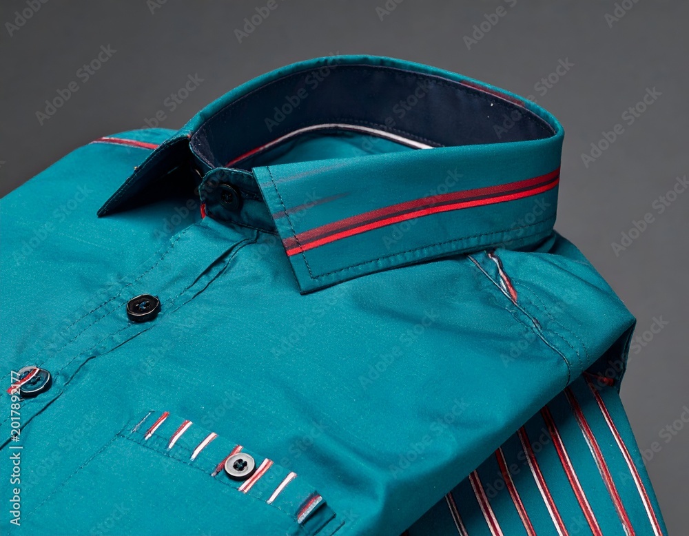 Naklejka premium Teal button-down shirt with a navy collar and red accent stripes, folded and angled against a gray backdrop