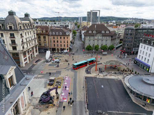 Aerial view of a city square featuring historic architecture, an articulated bus, and road construction under a cloudy sky in Biel Bienne, Canton of Bern, Switzerland.