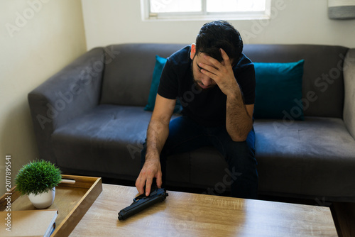 Schilderij op canvas Sad man contemplating difficult decision with handheld weapon, feeling hopelessn