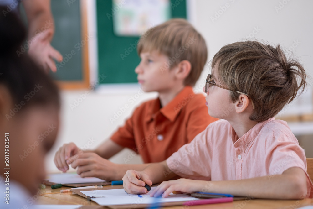 Fototapeta premium Teacher Helping Elementary Students with Drawing Activity in Classroom. Creative Classroom Lesson with Kids Coloring and Drawing, Education and Child Development in Modern Setting with boy, girl.