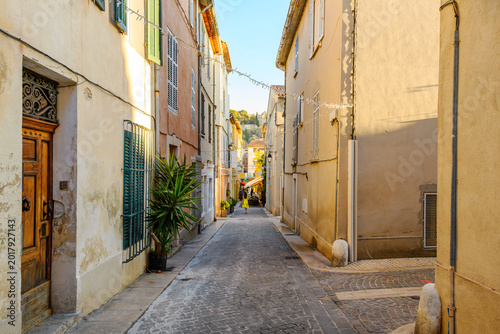 A young woman walks along a narrow residential cobblestone street of shops and sidewalk cafes towards the old town section of the seaside town of Cassis, France, French Riviera.