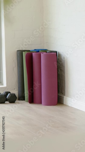 Vertical video: Recording rolled mats standing in home corner with hex weights on wooden floor