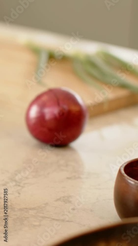 Vertical video: Pulling back camera revealing red onion on counter to reveal board, scallion, bowls