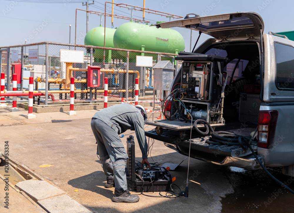 Fototapeta premium A field technician in industrial workwear unloading environmental air quality monitoring equipment and mobile sampling instruments from the back of a pickup truck at an industrial site.