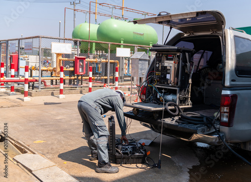 A field technician in industrial workwear unloading environmental air quality monitoring equipment and mobile sampling instruments from the back of a pickup truck at an industrial site.
