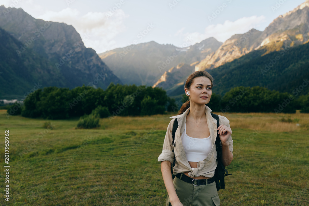 Obraz premium Woman with backpack exploring a landscape valley and mountains, outdoors in nature, hiking and adventure lifestyle in a meadow scene, smiling and confident.