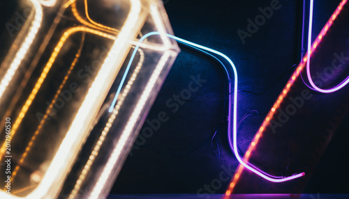 Close-up dynamic perspective of glowing neon light tubes mounted on a dark textured concrete wall, creating a moody and atmospheric cyberpunk interior aesthetic with vibrant purple and pink hues.