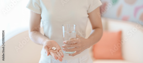 Bild auf Leinwand woman hand holding medicine painkiller pill and water glass on the sofa at home,