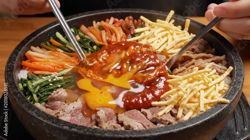 A close-up shot showcases a vibrant and meticulously arranged Korean bibimbap dish, with a raw egg nestled within a pool of gochujang sauce, ready to be mixed.
