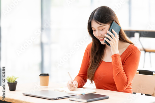 Happy Asian woman talking on phone while working in cafe