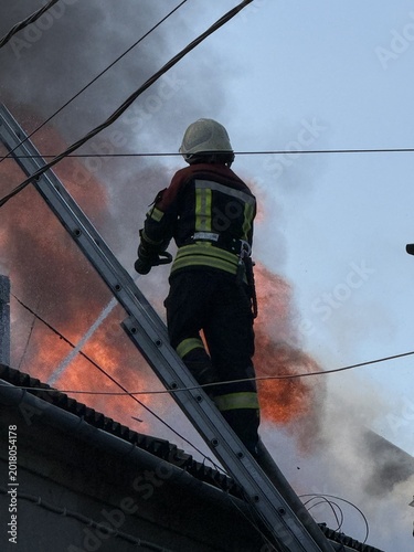Tablou pe pânză Firefighter battling a fierce house roof fire with a water hose