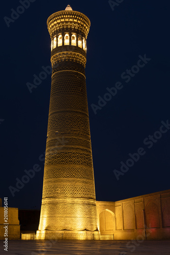 Fotografie Kalyan Minaret illuminated at night in Bukhara, Uzbekistan, with intricate brickwork patterns and warm golden lighting