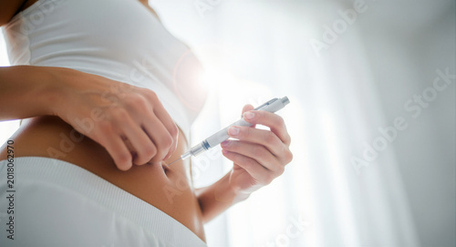 Woman injecting medicine into her abdomen using a medical pen. Patient self-administering treatment at home. Diabetes management concept, ideal for healthcare and medical wellness marketing.