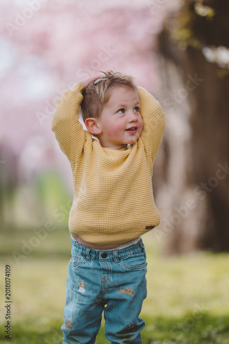 Kleiner Junge im Frühling unter blühenden Kirschbäumen im Park