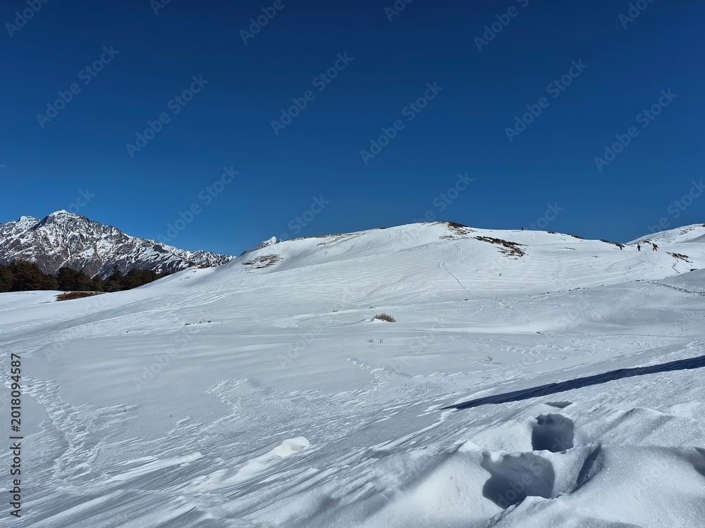 Fototapeta premium Miniature trekkers walking along a snowy ridge in the Himalayan wilderness of Gorson Bugyal