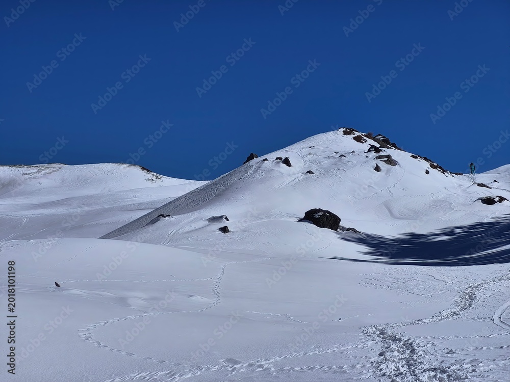 Fototapeta premium Expansive snow-covered ridge with footprints and wind patterns at Gorson Bugyal, Auli region.