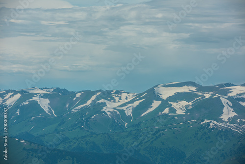 Foto Aerial top view above forest hills and big snowy mountain range in haze under clouds in changeable weather