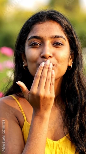 Attractive young Indian woman smiling and flying kiss outdoors in nature. Vertical video