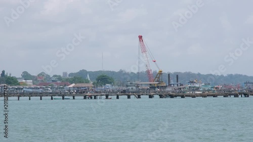 Industrial crane operating on the Ban Phe pier territory with boats, sea water and overcast sky visible in the background