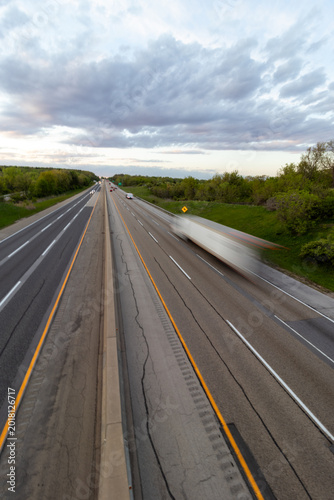 A slow shutter photo creating blur of a white semi truck with a black trailer driving down the highway road. 