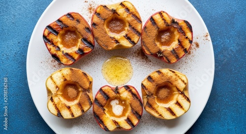 Grilled apple halves sprinkled with cinnamon and drizzled with honey on a white plate, top view of healthy warm dessert.