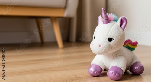 White unicorn plush toy with purple metallic details sitting on a wooden floor, cute soft stuffed animal in a modern home interior.