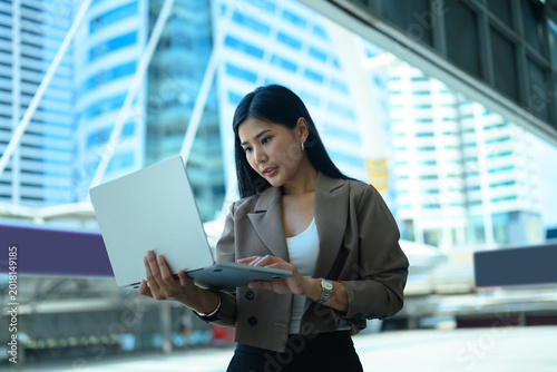 Bild auf Leinwand Young smiling Asian business woman wearing suit holding laptop computer standing