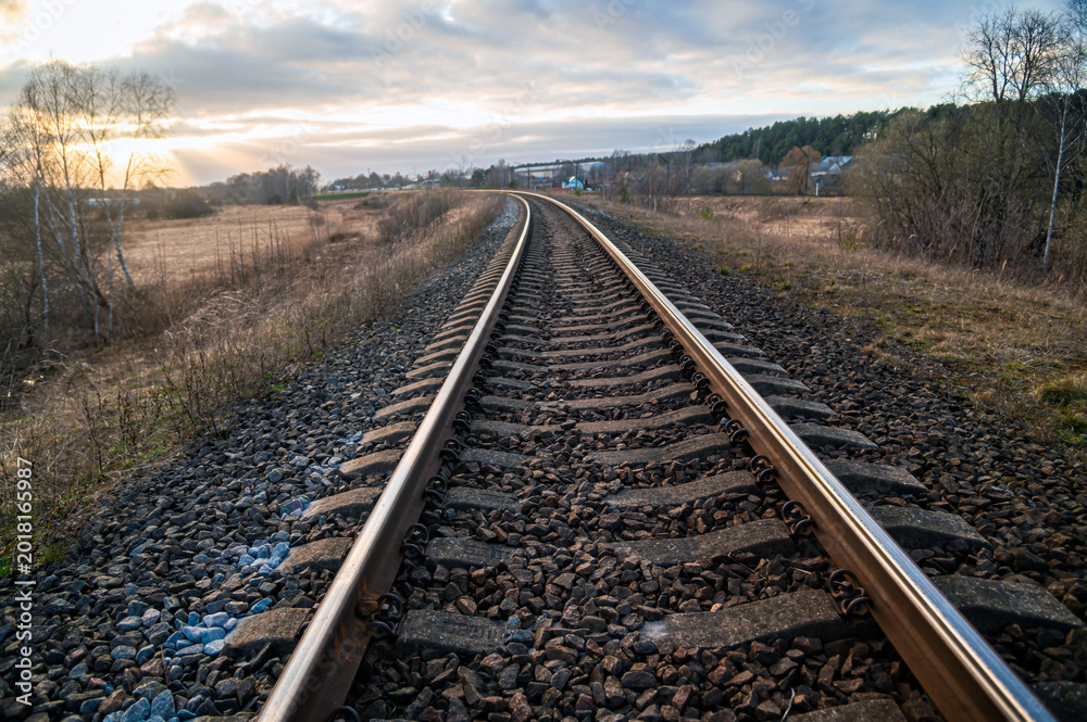 Obraz premium Railway tracks stretch through a quiet landscape during early evening light in the countryside