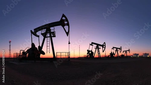 Silhouetted oil pumps against a vibrant twilight sky over an industrial landscape