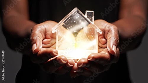 A translucent house filled with glowing light cradled between two hands