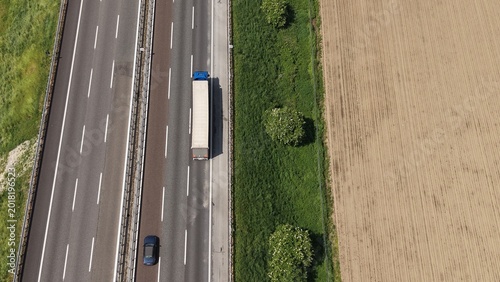 Highway Truck and Car Aerial View: An aerial perspective captures a truck and car traveling on a highway adjacent to agricultural fields under a clear sky.