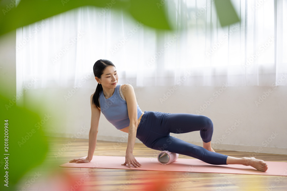 Fototapeta premium Asian Woman Using Foam Roller for Self-Massage in Yoga Wear