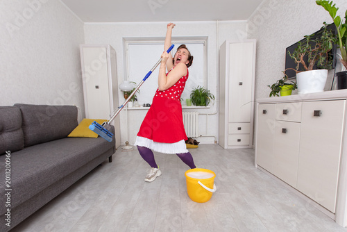 Fotografi Person in red dress acts as if singing while cleaning room with mop and bucket