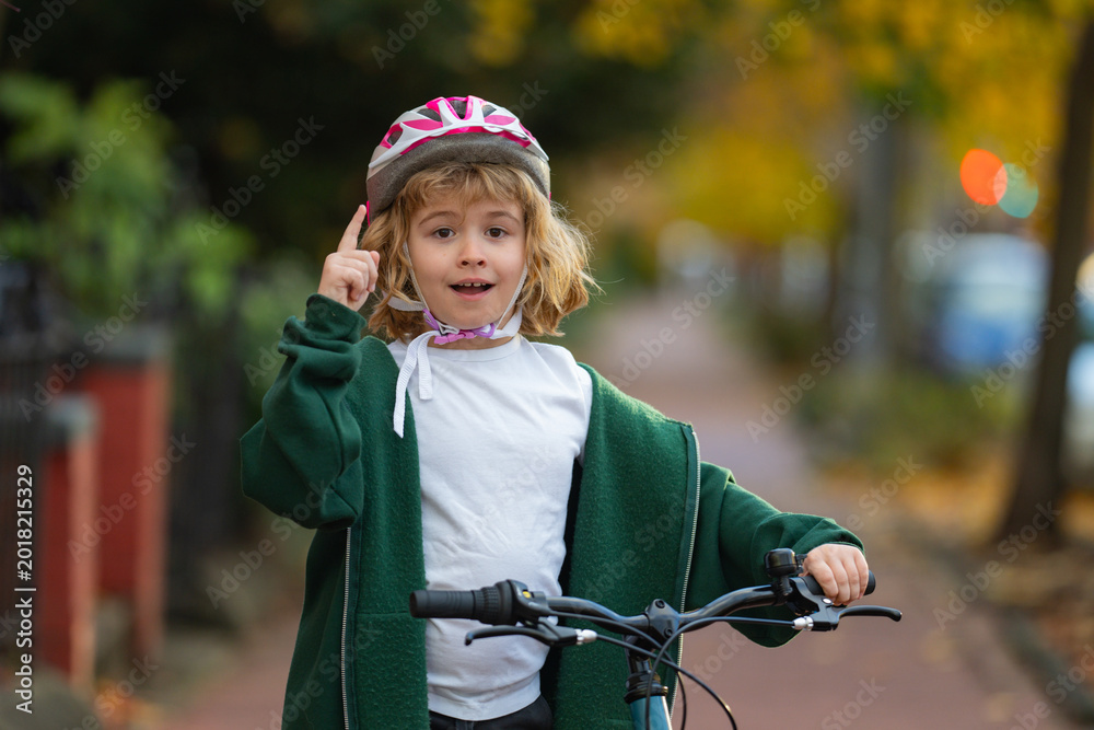 Naklejka premium Child rides bike on autumn. Kid portrait with bike helmet with idea. Safe kid cycling on street. Happy child learning to bike ride. Fun outdoor activity for children. Child with bicycle in autumn fall