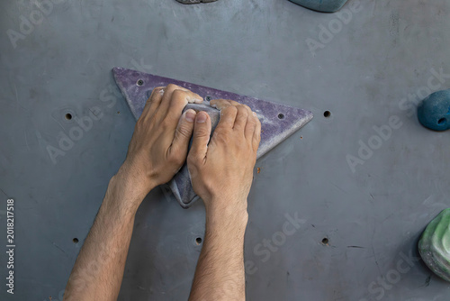 Climber gripping triangular hold on indoor climbing wall during bouldering practice. Concept of climbing technique, grip strength and endurance.