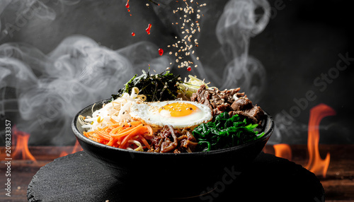 Fotografi makanan sinematik bibimbap korea dengan telur goreng daging sapi sayuran bayam tauge dan taburan wijen melayang dengan latar api