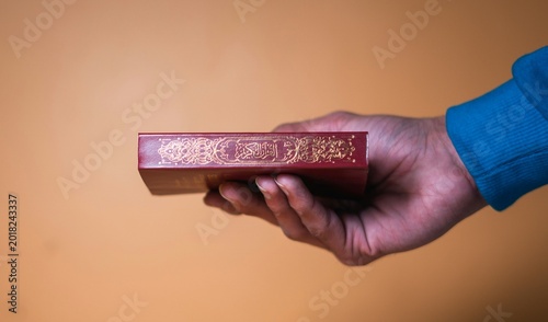 Photos Sacred Quran book, a holy Islamic scripture, held reverently in a hand, symbolizing faith and spiritual devotion, perfect for religious and cultural themes
