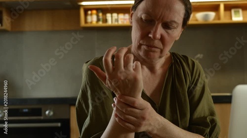 Mature woman massaging sore wrist near laptop at home workspace, discomfort from computer work and repetitive strain lifestyle concept. 4K.