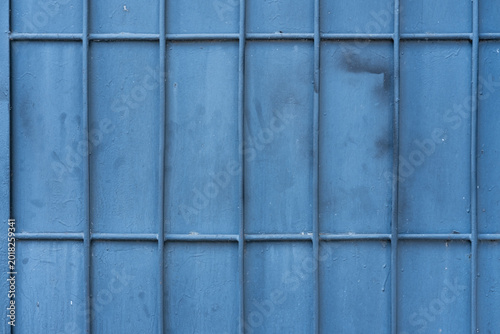Fotografia Metal gate painted in blue color displays vertical bars and horizontal lines with visible scuffs and dark marks