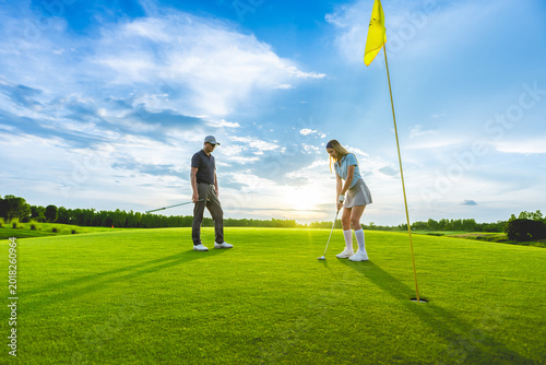 Foto Asian man and woman golfers swing clubs together on scenic golf course