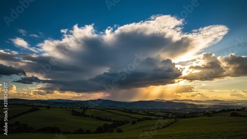 Epic cloudscape at sunset with bright sun rays shining over rolling green hills and distant mountains
