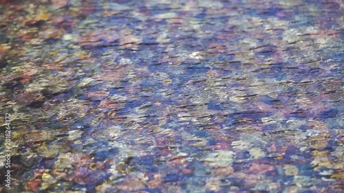 Extreme close-up of sparkling river water surface with bright sun reflections and colorful stones visible through the clear liquid.