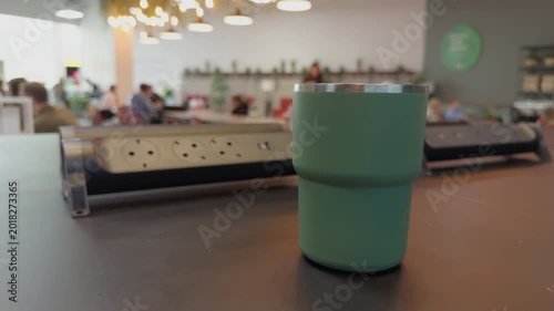 Reusable cup amidst lively cafe scene. Sustainable travel mug captures cozy social setting