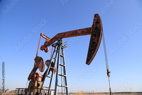 Tablou pe pânză Rusted Red Oil Pump Jack Against Clear Blue Sky