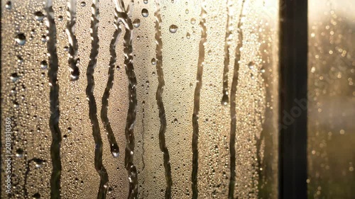 Water droplets and streaks on glass window with soft golden hour sunset light, creating a textured background effect