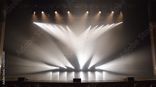 Empty performance stage with rustic wooden floorboards illuminated by moving white spotlights and smoke effects.