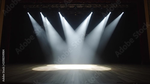 Empty performance stage with rustic wooden floorboards illuminated by moving white spotlights and smoke effects.